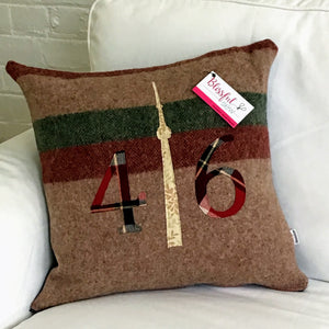 Light brown pillow with maroon and moss stripes. Maroon plaid numbers and cream CN Tower.